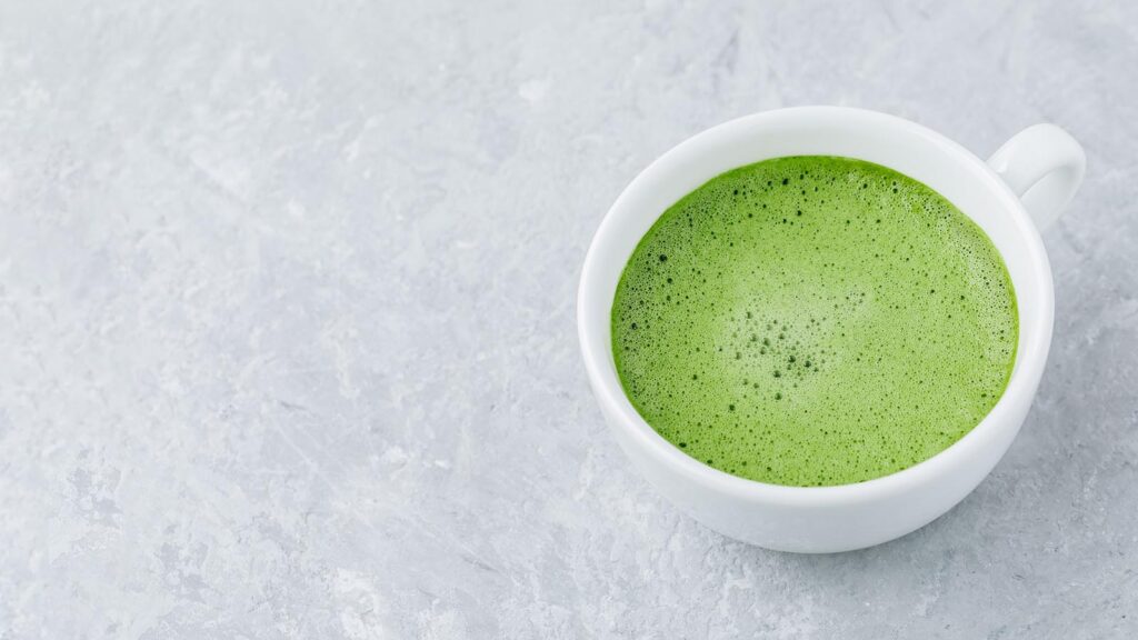 Japanese matcha green tea latte in white cup on gray stone background.