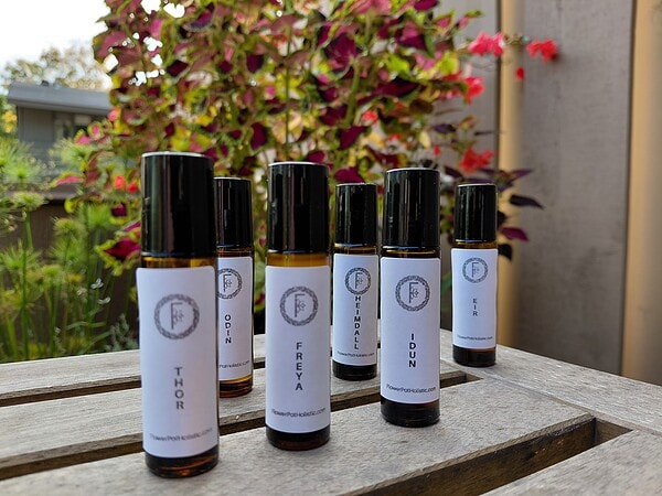 Relaxing essential oils for aromatherapy with labels displaying various blends on glass bottles, set outdoors with vibrant pink and purple flowers in the background.