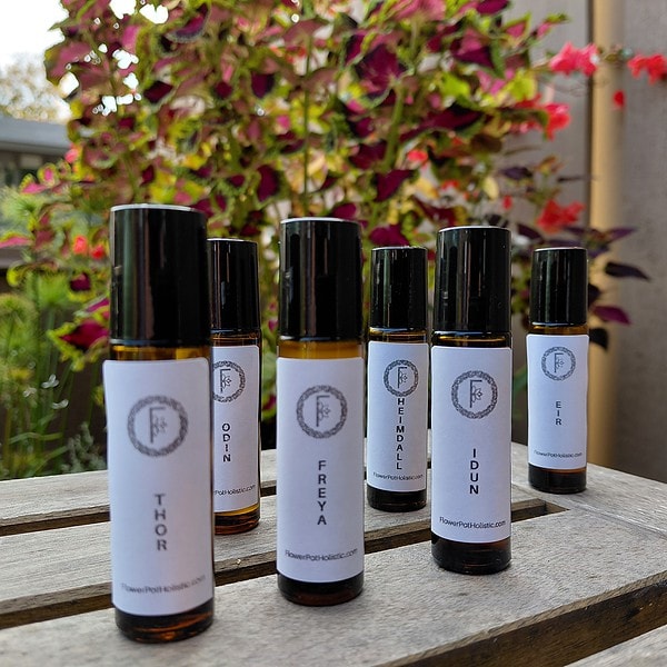 Relaxing essential oils for aromatherapy with labels displaying various blends on glass bottles, set outdoors with vibrant pink and purple flowers in the background.