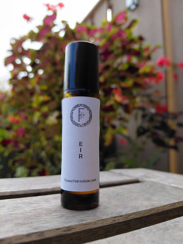 Aromatherapy essential oil roller bottle with minimalist label on wooden surface, outdoors lush garden background, emphasizing natural wellness and holistic health products.