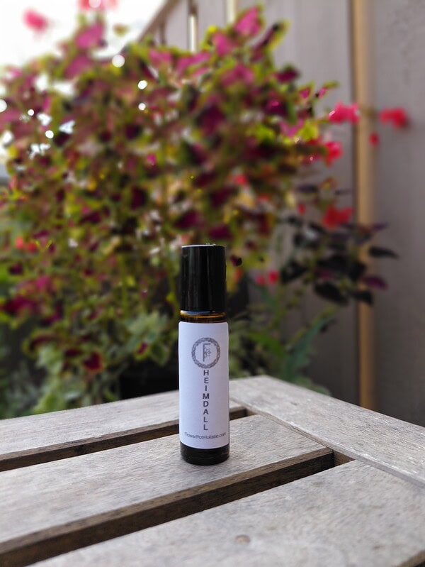 Hemp essential oil bottle with a white label on a wooden surface, green and pink flowering plant in the background, outdoor setting, natural light, herbal wellness product, aromatherapy, holistic health, Flower Pot.