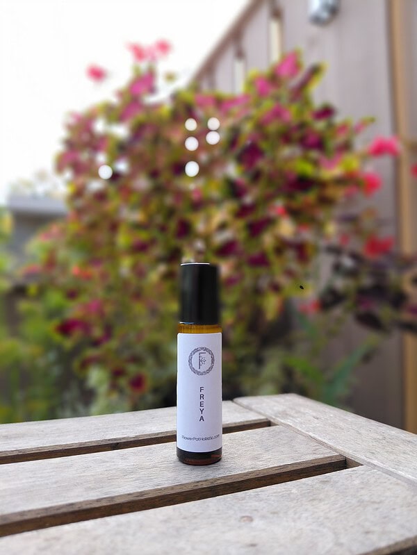 Lavender essential oil bottle on a weathered wooden table with a blooming pink and purple flower bush in the blurred background. Perfect for aromatherapy, natural wellness, and holistic health.
