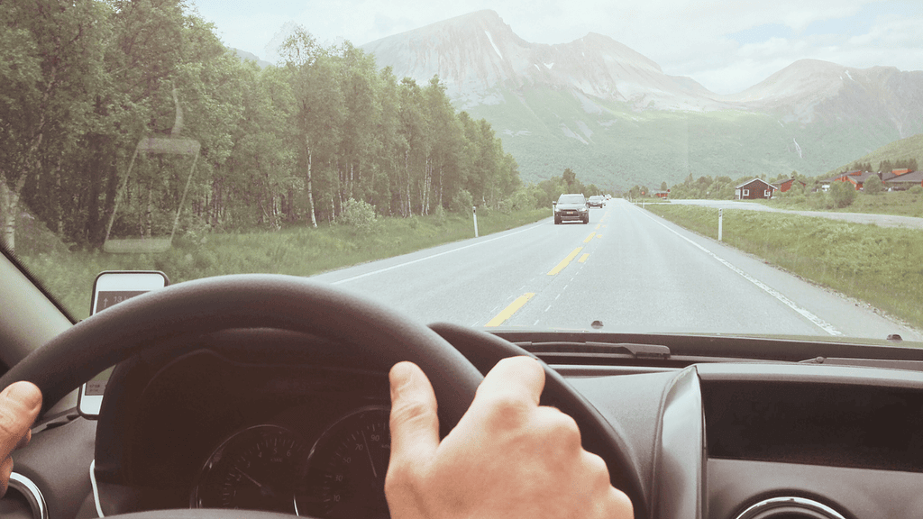 A peaceful highway scene with lush green trees and towering mountains in the distance, captured from inside a vehicle. Ideal for travel, nature, and adventure-related content.