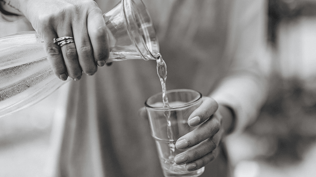 A person pouring fresh water into a glass, emphasizing hydration and wellness. Perfect for promoting healthy living and natural health remedies.