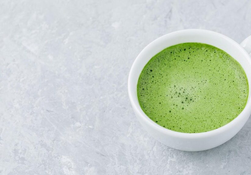 Japanese matcha green tea latte in white cup on gray stone background.