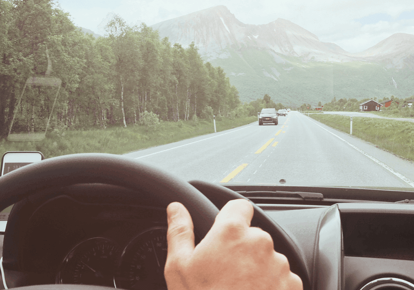 A peaceful highway scene with lush green trees and towering mountains in the distance, captured from inside a vehicle. Ideal for travel, nature, and adventure-related content.